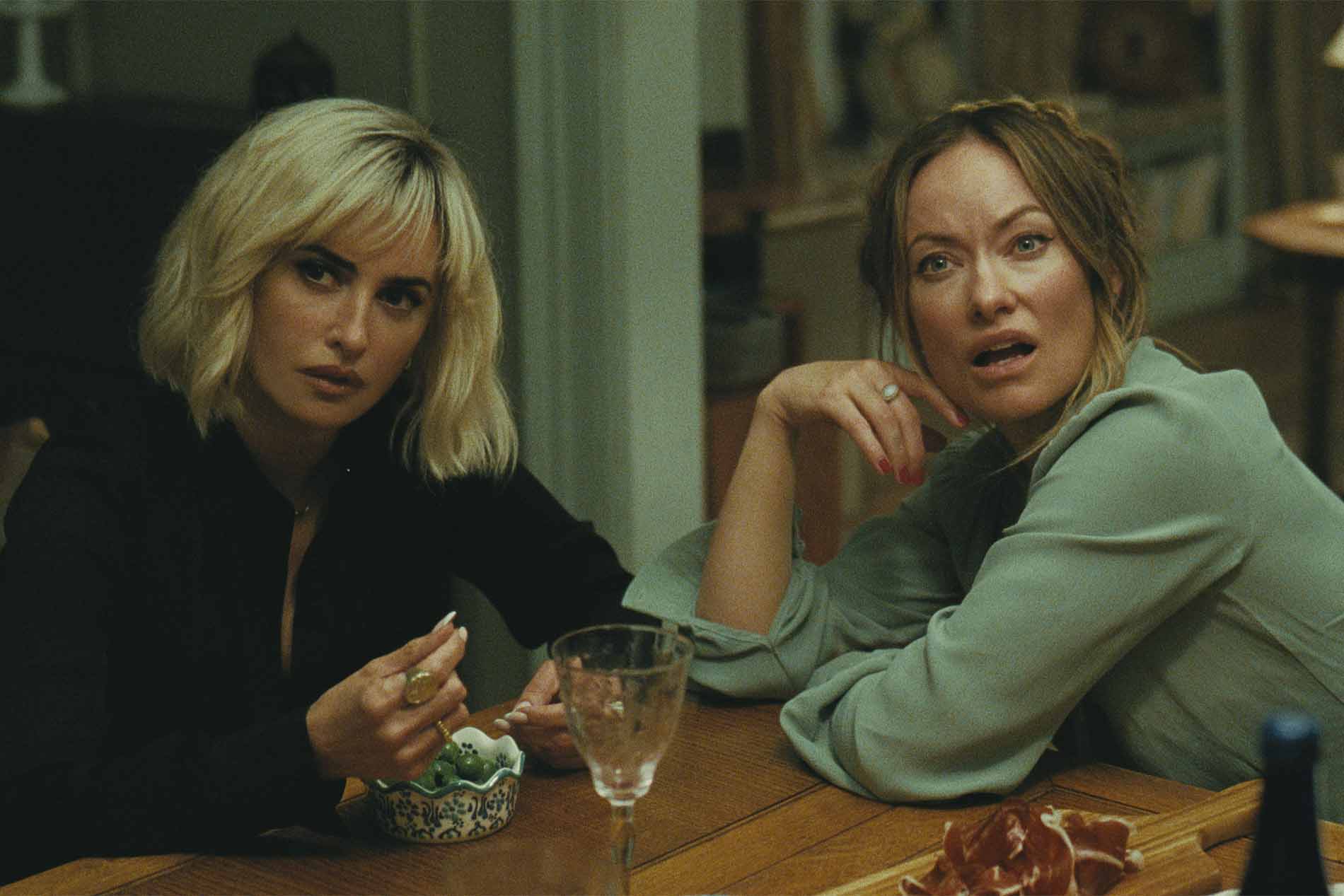 Scena di The Invite - Il Piacere è Tutto Nostro: Penélope Cruz e Olivia Wilde sedute a tavola durante la cena, tra bicchieri di vino e antipasti.