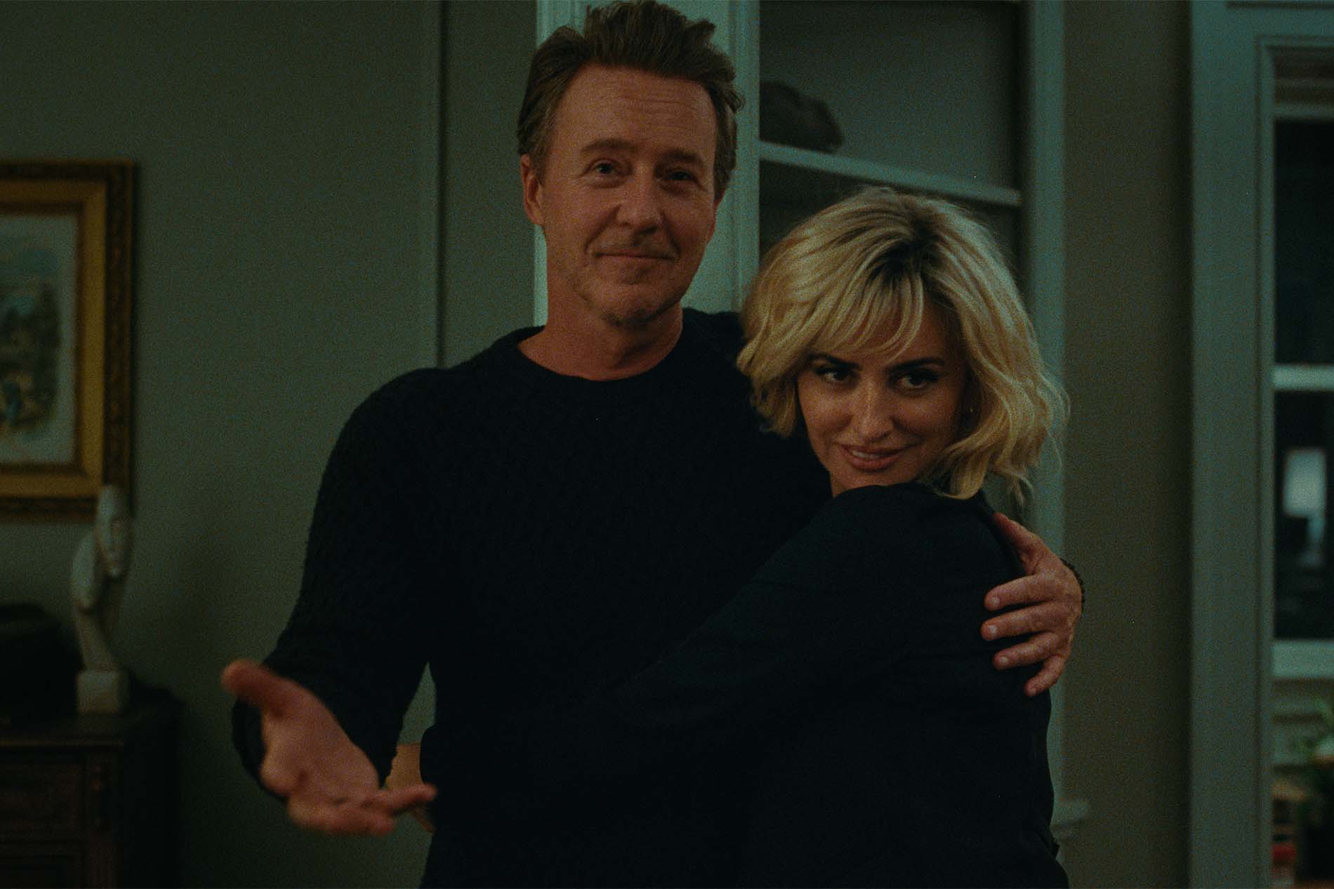 Scena di The Invite - Il Piacere è Tutto Nostro: Edward Norton abbraccia Penélope Cruz in salotto, entrambi sorridenti.
