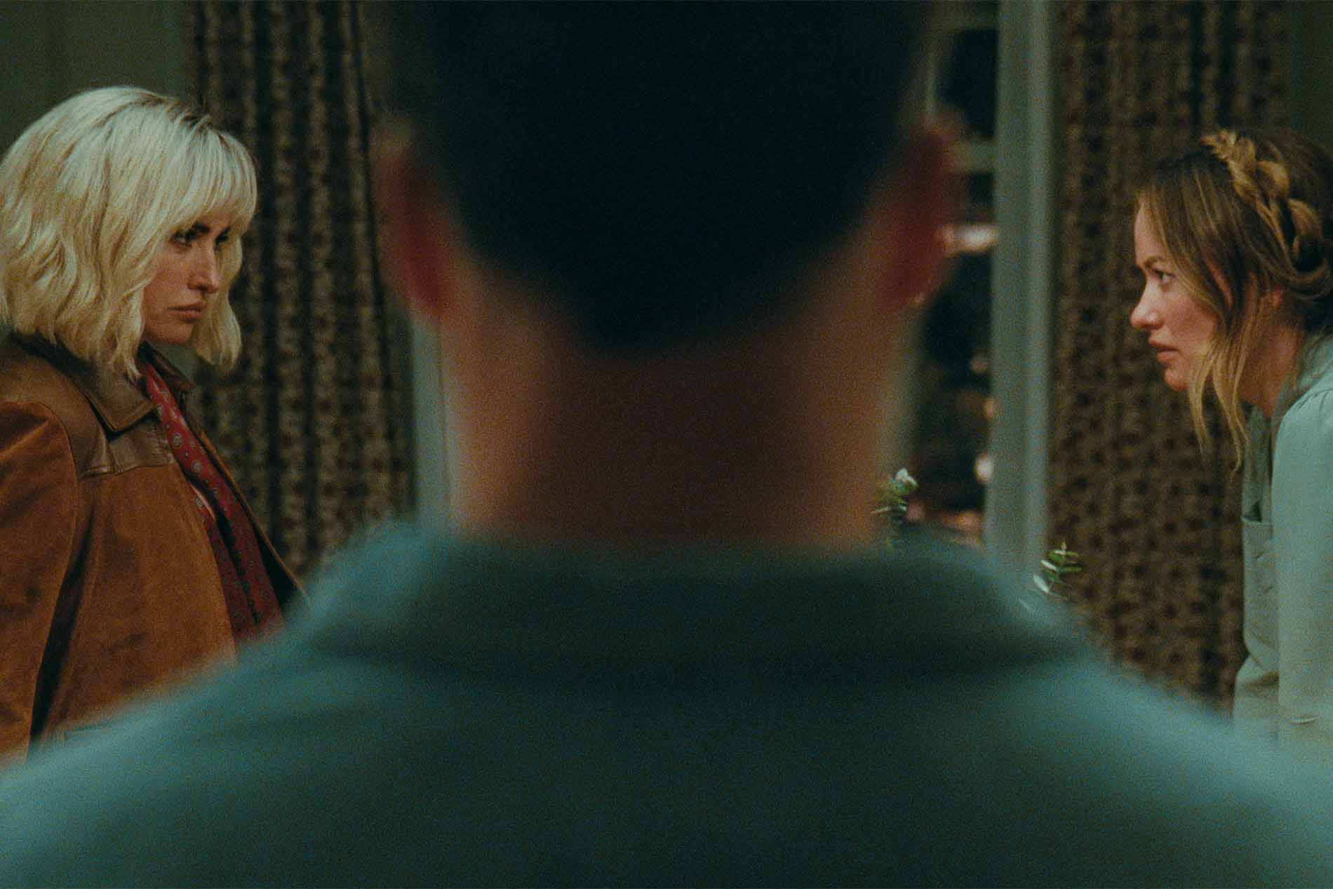 Scena di The Invite - Il Piacere è Tutto Nostro: Penélope Cruz e Olivia Wilde si scambiano uno sguardo perplesso davanti a un uomo ripreso di spalle.