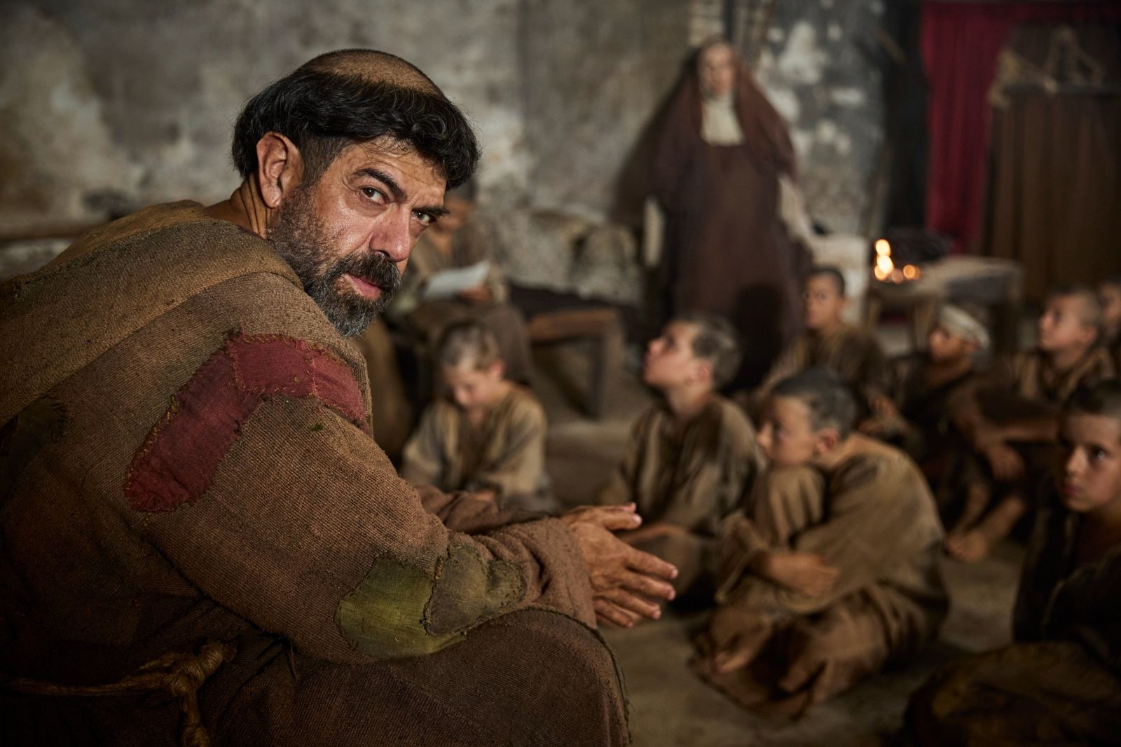 Frate Leopoldo, seduto tra un gruppo di bambini vestiti di sacco, si volta a guardare verso l’obiettivo; sullo sfondo, una suora.